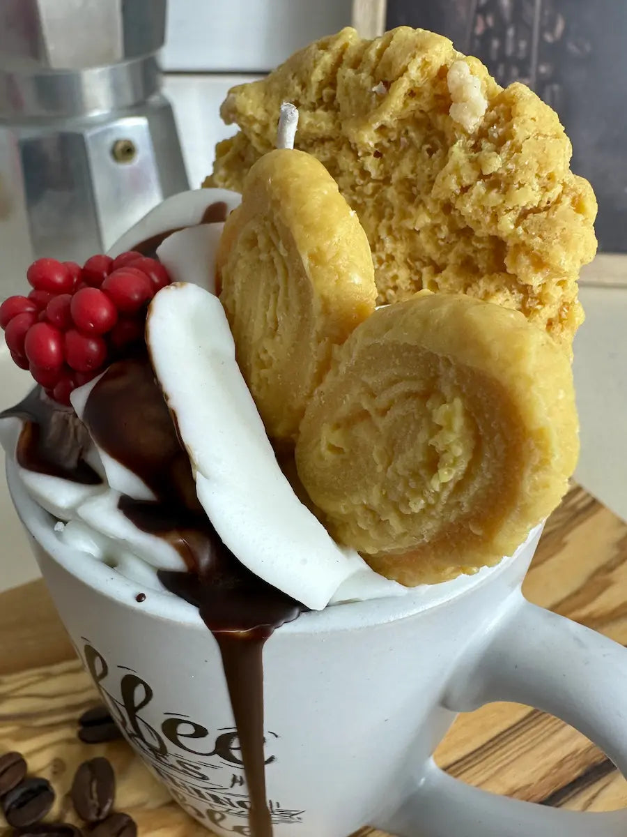Schrägaufnahme der Duftkerze „Coffee Makes Everything Possible“ mit cremiger Wachsoptik und Gebäck-Topping – kramMITcharme