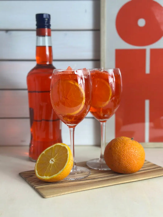 Handgemachte Duftkerze Aperol Spritz mit zwei Gläsern, Orangen und Flasche im Hintergrund – kramMITcharme
