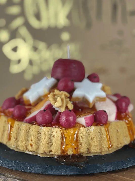 Nahaufnahme der Duftkerze „Bratapfel Royale“ mit roten Beeren, weißen Sternen, Apfelscheiben und karamelligem Guss – kramMITcharme