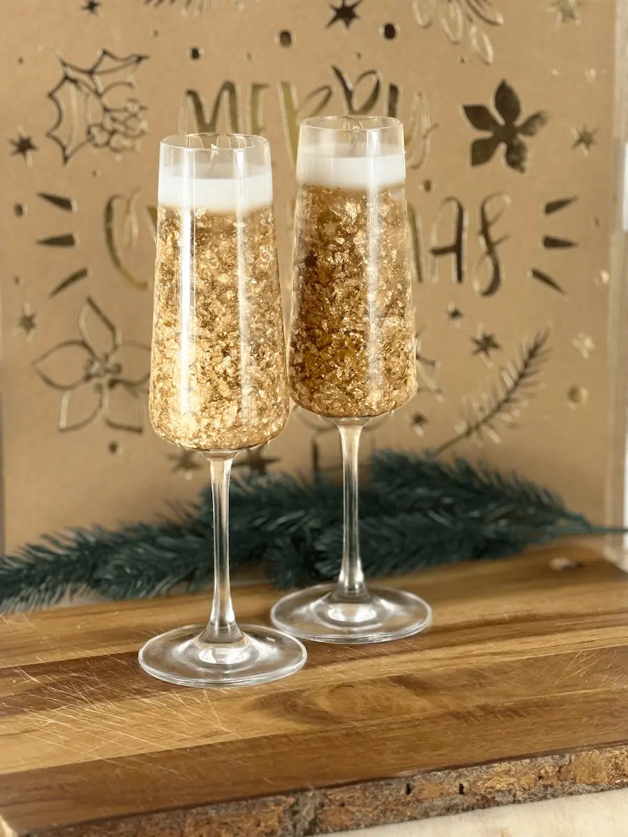 Handgemachte Dessertkerze im Champagnerglas mit goldenen Sprudelelementen auf Holzbrett vor festlicher Deko – kramMITcharme