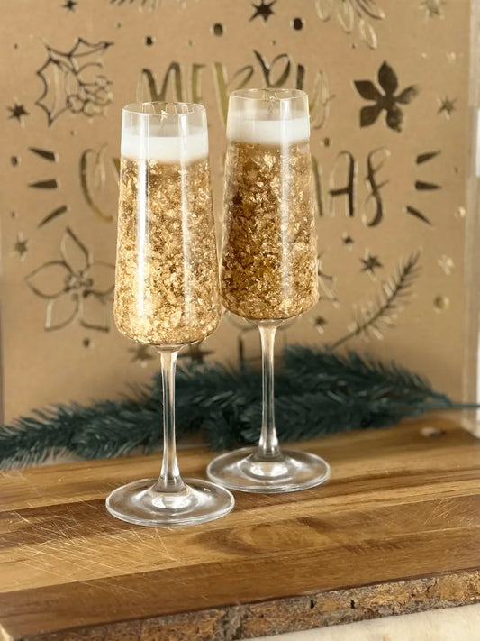 Handgemachte Dessertkerze im Champagnerglas mit goldenen Sprudelelementen auf Holzbrett vor festlicher Deko – kramMITcharme