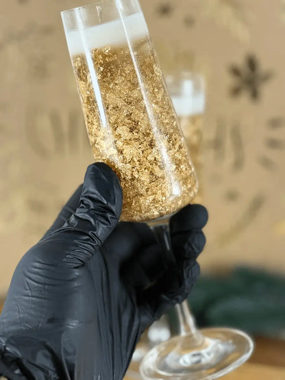 Nahaufnahme der Champagnerlicht-Kerze im Sektglas, gehalten von einer schwarzen Handschuhhand, mit goldenen Details – kramMITcharme