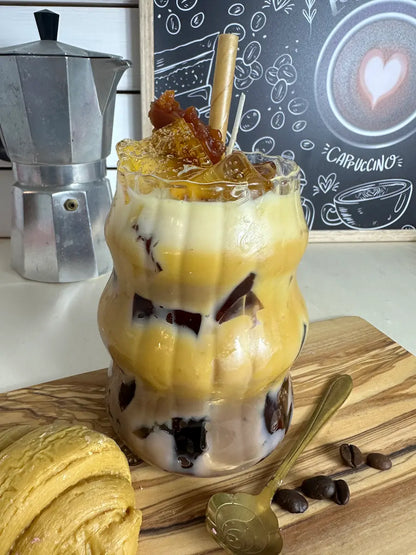 Dessertkerze im Latteglas mit marmorierten Wachsschichten, Schokoeinschlüssen und Schaumschicht vor Caféhintergrund – kramMITcharme