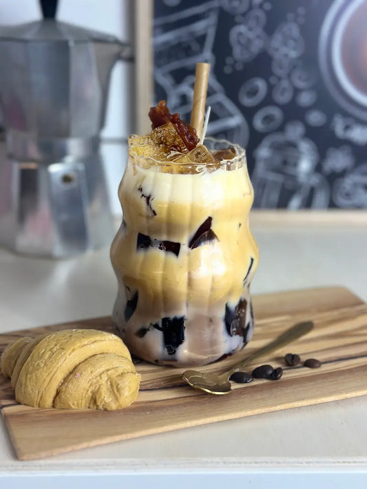 Handgemachte Dessertkerze im Latteglas mit hell-dunklem Schichtwachs, Milchschaum und Deko auf Holzbrett – kramMITcharme