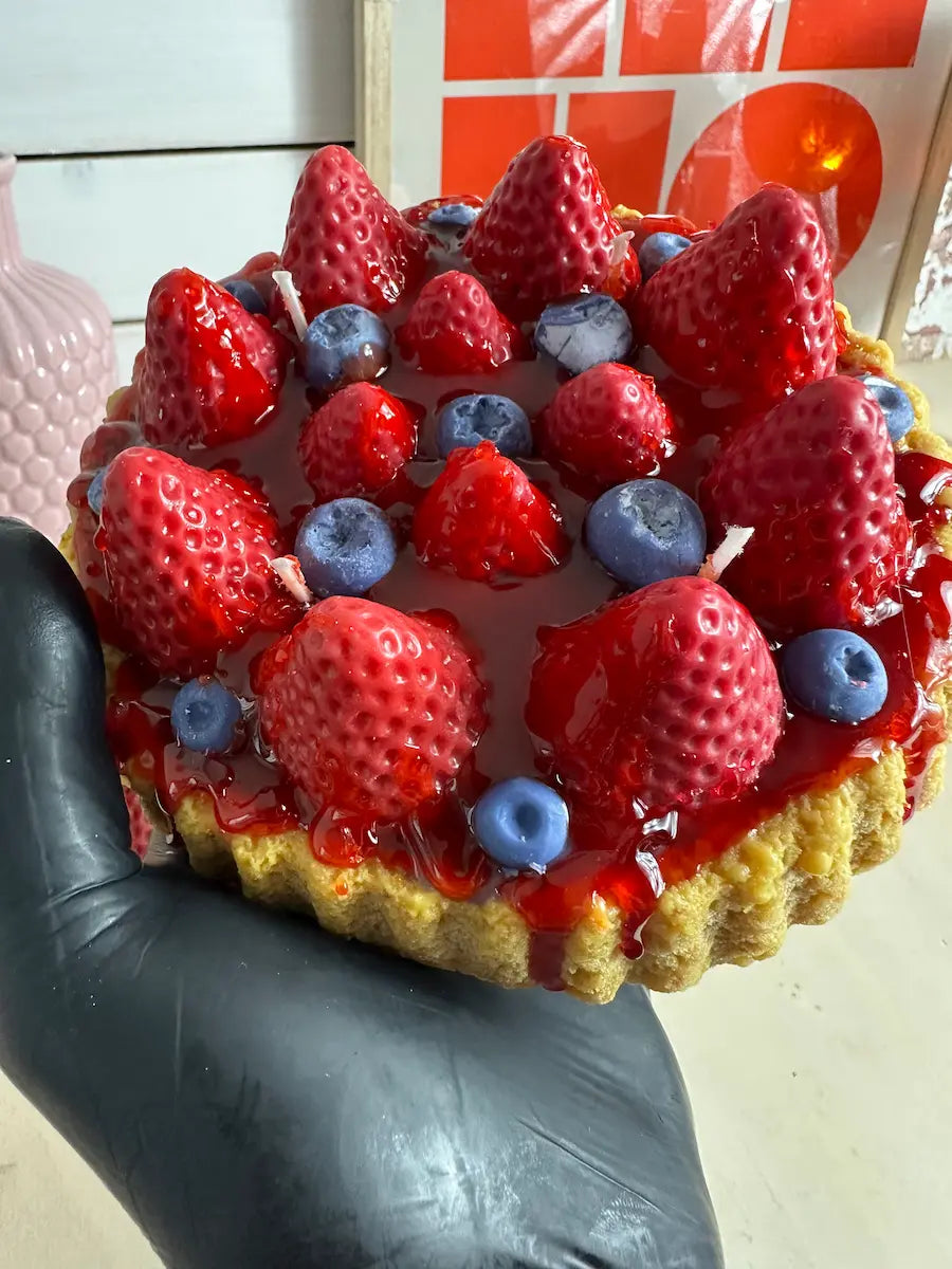 Handaufnahme der Duftkerze „Erdbeerkuchen“ mit Erdbeer- und Blaubeer-Deko auf Keksboden – kramMITcharme