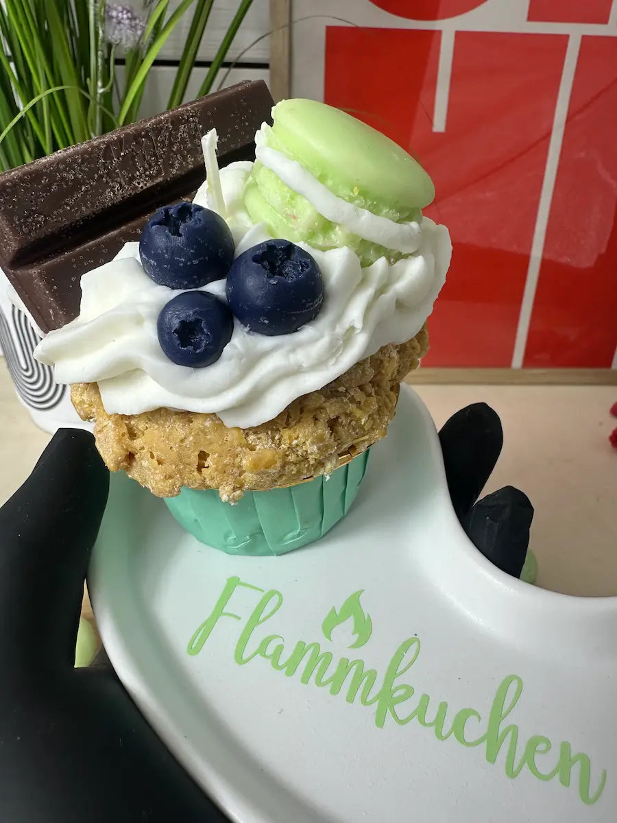 Handaufnahme der Duftkerze „Flammkuchen Cupcake“ mit Dessertoptik, Blaubeeren und Macaron – kramMITcharme
