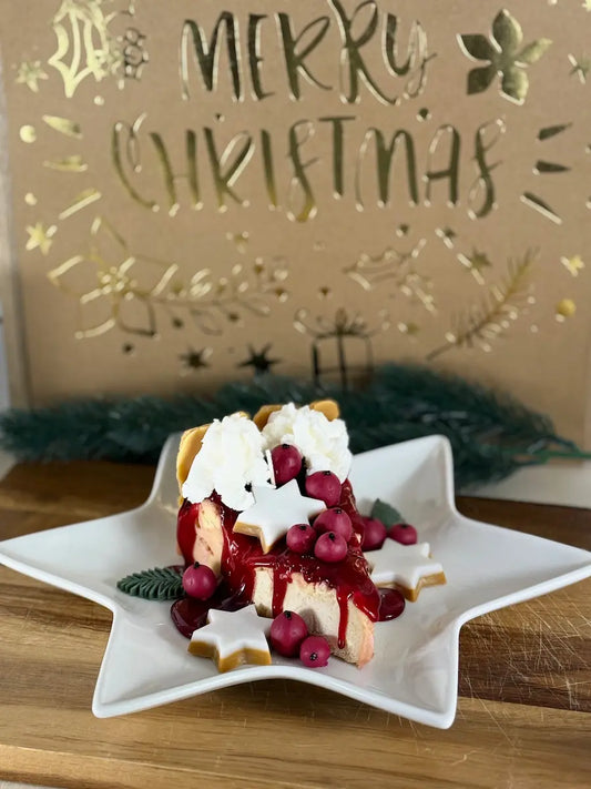 Handgemachte Duftkerze „Glühwein-Cheesecake Deluxe“ als Kuchenstück auf weißer Sternplatte mit Baiserhaube, Glühweinbeeren und winterlichen Deko-Elementen – kramMITcharme