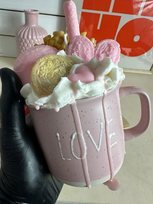 Handaufnahme der Duftkerze „Love Coffeecup“ mit zarter Herzdeko, rosa Keks und Sahnetopping aus Wachs – kramMITcharme